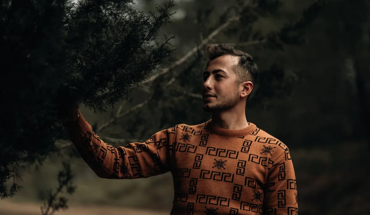 Homme en pull rouille à motifs géométriques qui touche une branche de sapin en forêt